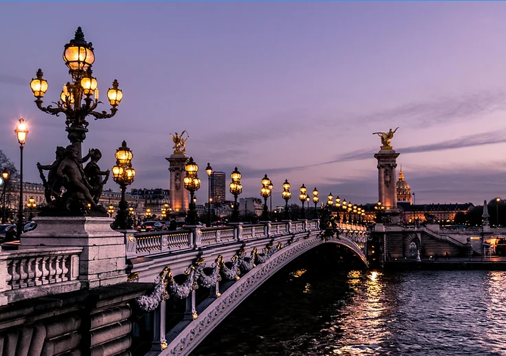 A beautifully lit bridge in Paris at dusk with ornate lamp posts and statues.